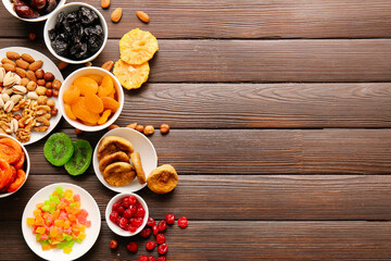 Bowls with different dried fruits and nuts on wooden background
