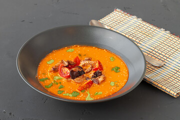 Tom Yam Thai soup in black bowl on gray table