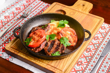 Close up of juicy beef steak served in a pan with bbq grilled tomatoes over traditional Ukrainian tablecloth.