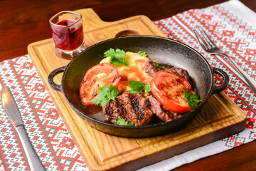 Close up of juicy beef steak served in a pan with bbq grilled tomatoes over traditional Ukrainian tablecloth.