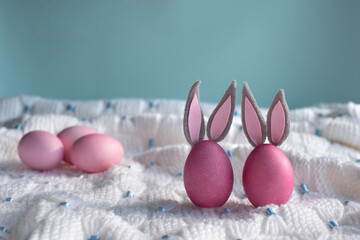  Two pink Easter eggs with bunny ears close-up on a white knitted plaid and blue background