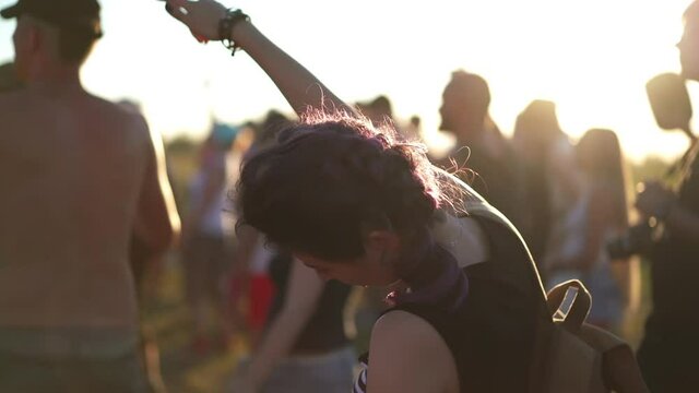 Music fans enjoying summer gig. Concept of youth culture and entertainment. Pretty asian woman dancing at sunset light among the crowd of people at rock concert festival.