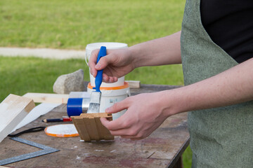 A young male designer paints a wooden Board white with a brush. The young man is working near his house. 