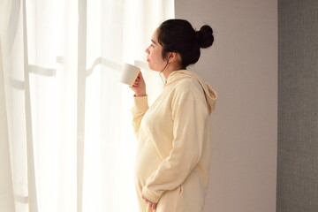 A pregnant woman in her twenties is drinking a drink in a mug. 