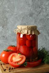 Board with jar of pickled tomatoes on wooden table