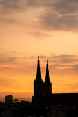 Beautiful red and blue sunrise sky with clouds over black silhouette of city with tower of church on horizon. Silhouette of the catholic church and cross