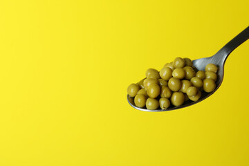 Spoon with peas beans on yellow background