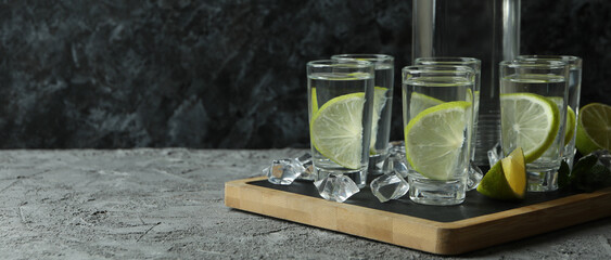 Fototapeta na wymiar Board with bottle and shots of vodka with lime on gray table