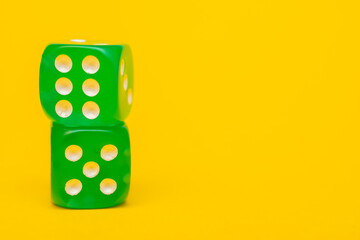 Two green dice show six and five, lying on top of each other on a yellow background with space for text: side view. Concept of board table games for the whole family