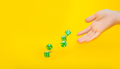 A lot of green dice fall from the hand on a yellow background with space for text: board games, selective focus on the hand, a photo in motion