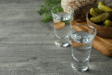 Shots of vodka, pickles, bread and dill on gray table