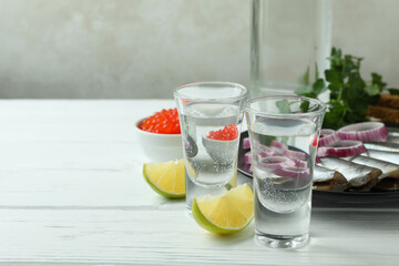 Shots of vodka and tasty snacks on white wooden background, space for text