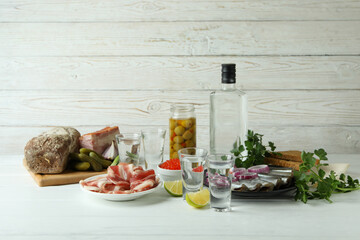 Shots of vodka and tasty snacks on white wooden background