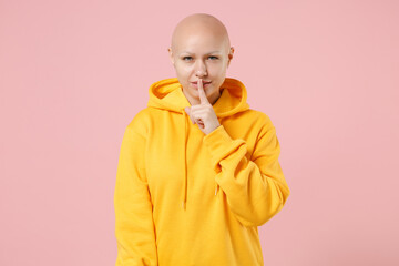 Young bald caucasian secret woman 20s without hair wearing yellow casual sweatshirt shirt say hush be quiet with finger on lips shhh gesture isolated on pastel pink color background studio portrait.