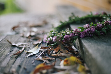 Symbolism between summer and autumn: a braided wreath of clover flowers lies on wooden boards covered with yellowed leaves. Background