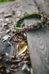 Symbolism between summer and autumn: a braided wreath of clover flowers lies on wooden boards covered with yellowed leaves. Background