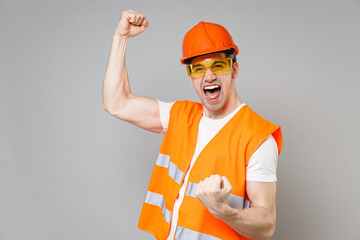 Young employee happy man in orange vest protective helmet hardhat do winner gesture clenching fist...