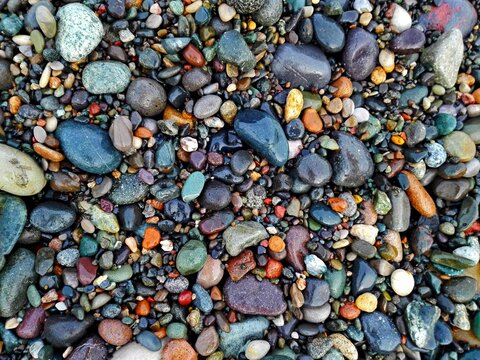 Colorful Sea Pebble stones rocks wet on beach. Different forms multicolor Pebbles stone (green, orange, grey, black) as natural rock abstract texture background. Close up rock colorful pebble stones