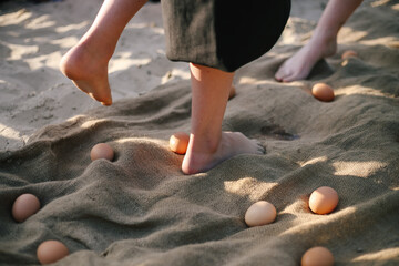 Many chicken eggs lie on burlap and are scattered on the sand. Conceptual photo