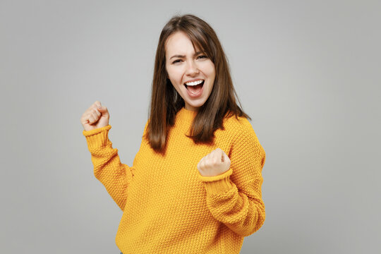 Young excited happy overjoyed attractive beautiful woman in casual knitted yellow sweater do winner gesture clench fist say yes isolated on grey background studio portrait People lifestyle concept