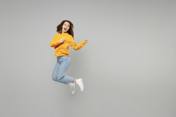 Fototapeta na wymiar Full length of young excited overjoyed expressive woman in knitted yellow sweater run fast in air jump high point index finger aside on workspace mock up isolated on grey background studio portrait..