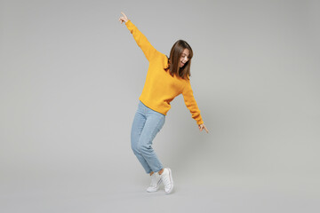Full length of young relaxed positive student caucasian happy satisfied woman 20s wearing knitted yellow sweater leaning over with outstretched isolated on grey color background studio portrait..