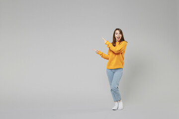 Full length of young smiling positive caucasian happy woman 20s in knitted yellow sweater stand point index finger aside on workspace copy space area isolated on grey color background studio portrait - obrazy, fototapety, plakaty