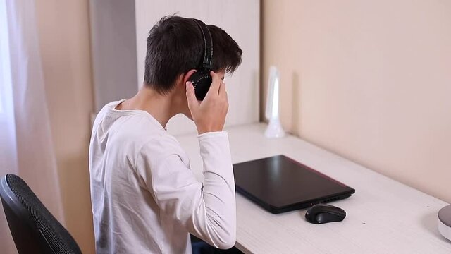 Process of teenage boy puts on headphones befour starting play games. Side view of boy preparing for gaming