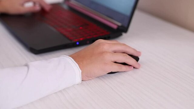 Closeup of teenage boy playing game on his pc computer in white room. Gamer capture video on web camera on laptop. Focus on hand with computer mous