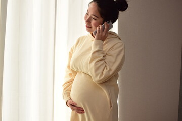 A pregnant woman in her twenties is calling on her smartphone. 