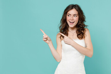 Excited funny bride young woman 20s in beautiful white wedding dress point index finger aside up isolated on blue turquoise color wall background studio portrait. Ceremony celebration party concept.