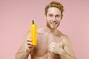Fototapeta premium Smiling bearded naked young man 20s perfect skin hold empty blank bottle of shampoo showing thumb up isolated on pink background studio portrait. Skin care healthcare cosmetic procedures concept.