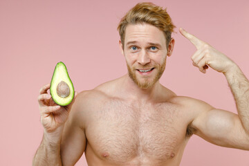 Smiling bearded naked young man 20s perfect skin hold half fresh avocado fruit point index finger...