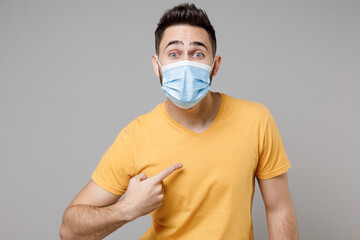 Young shocked surprised man in yellow t-shirt in sterile face mask safe coronavirus covid-19 pandemic quarantine put hand on forehead head having headache isolated on grey background studio portrait.