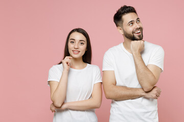 Young pensive couple two friends bearded man brunette woman in white basic blank print design t-shirts thinking dream put hand prop up on chin isolated on pastel pink color background studio portrait.