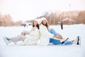 Obraz premium Young happy women in winter with skates on open air ice rink. Girl friendship concept