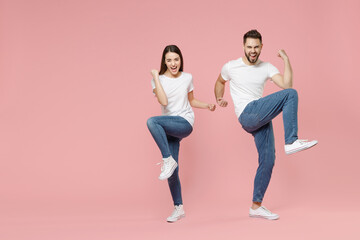 Full body length young cheerful fun couple two friends bearded man brunette woman in white basic blank print design t-shirts jeans celebrating isolated on pastel pink color background studio portrait.