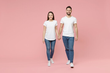 Full body length young cheerful couple two friends bearded man brunette woman in white basic blank print design tshirt jeans walk go move step isolated on pastel pink color background studio portrait