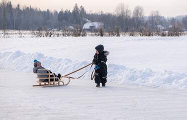 Happy children on a winter lake, playing together with a sledge while snowing. Childhood happiness concept