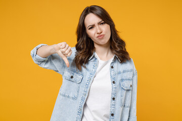 Young dissatisfied displeased sad caucasian brunette woman 20s in casual stylish denim shirt white t-shirt show thumb down dislike gesture disagree isolated on yellow color background studio portrait