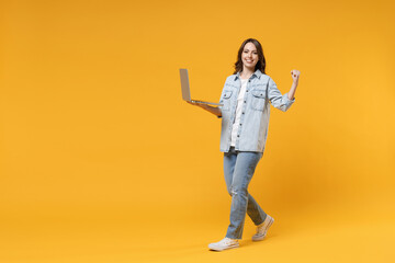 Fototapeta na wymiar Full length of young freelancer copywriter excited successful happy woman in denim shirt white t-shirt hold laptop computer do winner gesture clench fist isolated on yellow background studio portrait.