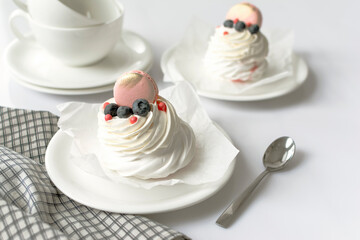 Still life Pavlova meringue cake decorated macaron on white background. Tea cups and napkin on wood table