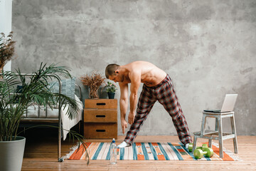 The young man goes in for sports at home. Sportsman with black hair in home pajamas  does morning...