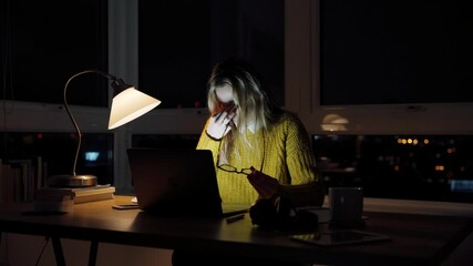 Female caucasian student working late at night rubbing eyes tired typing on laptop sitting at desk