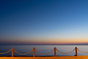 beachfront sidewalk illuminated by street lights and a calm ocean sunset behind