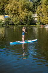 Fototapeta na wymiar Charm young woman on paddle board SUPat the city lake