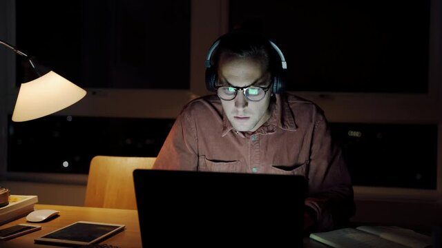 Caucasian male free lancer working late at night eating foot sitting typing on laptop 
