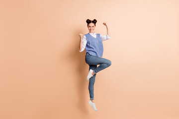 Fototapeta na wymiar Full length photo of charming lucky young lady wear blue vest jumping high rising fists isolated beige color background