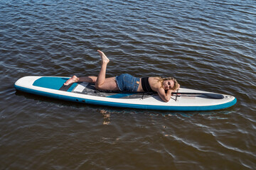 Young female surfer lying on sup board and rest at nature
