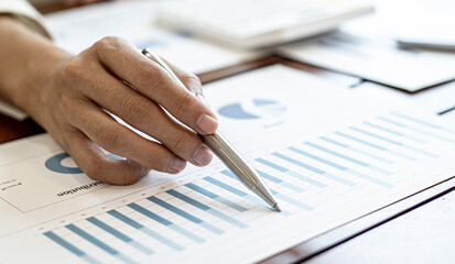Close-up businesswoman's hand holding a pen pointing at a bar chart on a corporate financial information sheet, the businesswoman examines the financial information provided by the finance department.